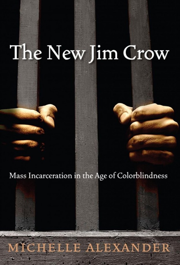 The cover of the book "The New Jim Crow" by Michelle Alexander. A pair of Black hands grip vertical wooden bars against a dark background.